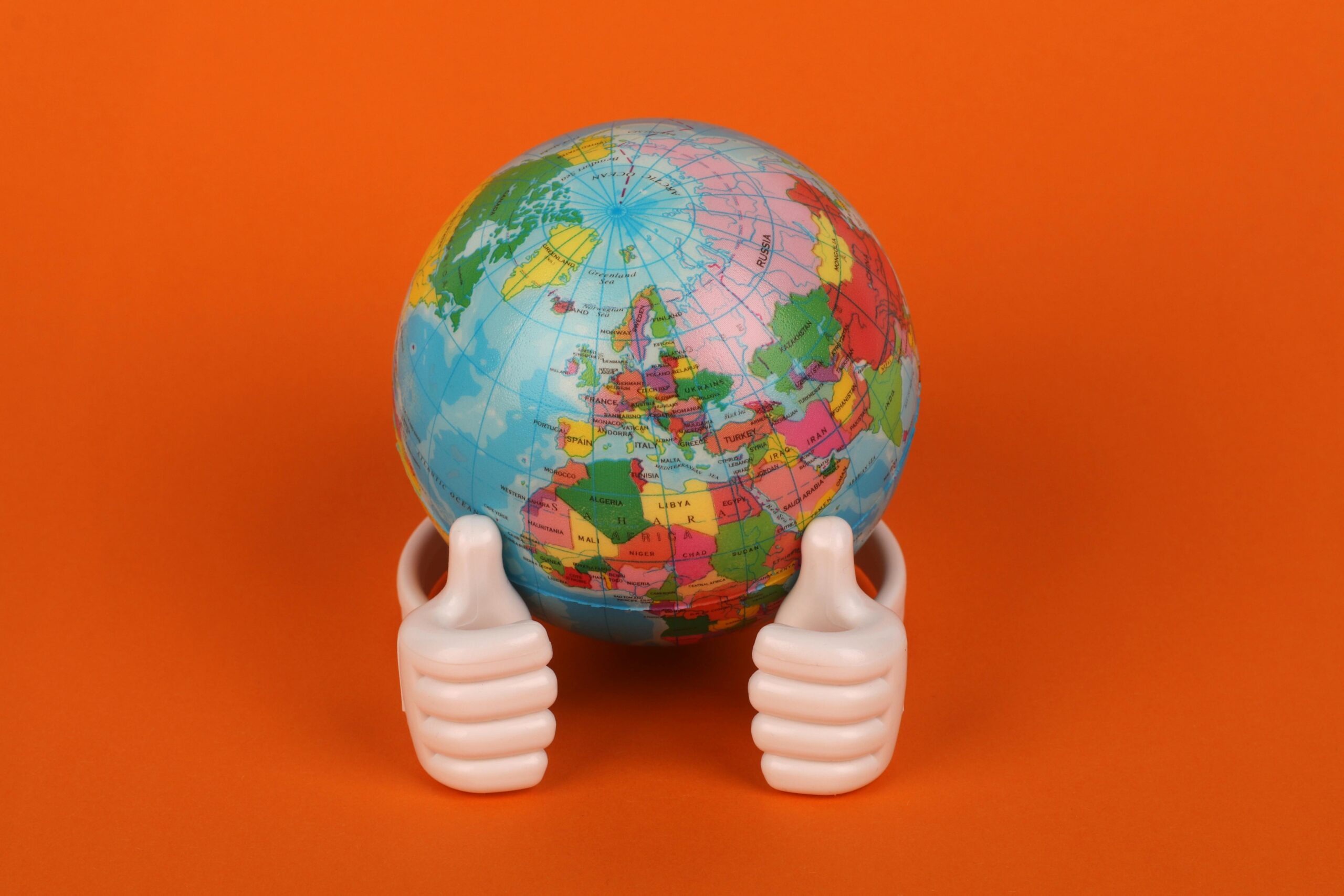 Vibrant globe model with thumbs-up figurines on orange background, symbolizing global positivity.