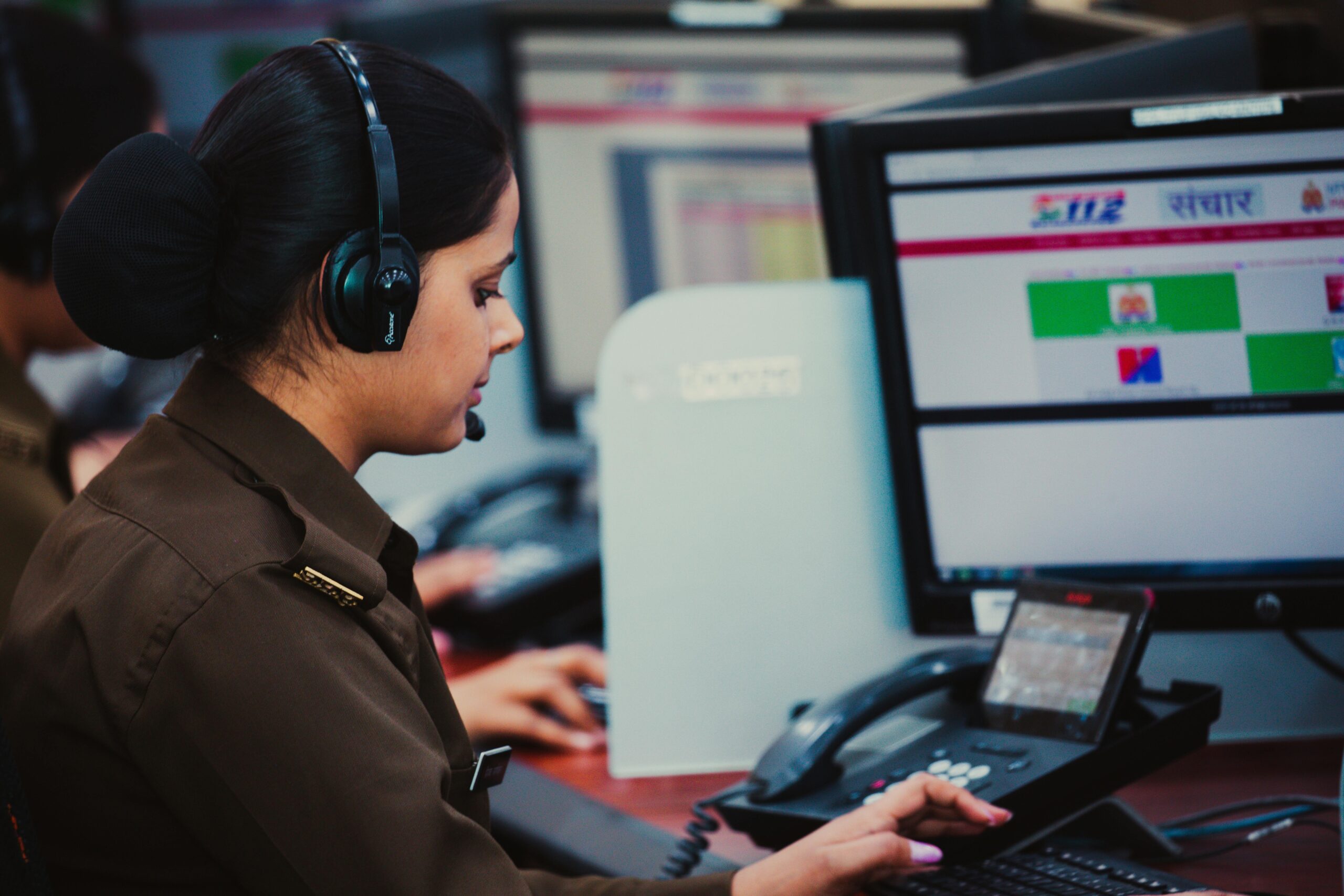 Focused call center dispatcher in uniform using computer and headset in office environment.
